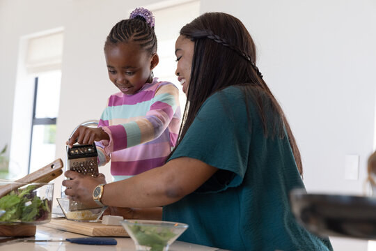African American mother and child grating cheese at kitchen island using box grater, glass bowl