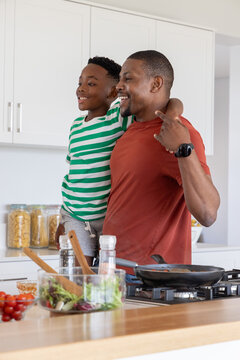 African American father holding son preparing meal at kitchen island with frying pan