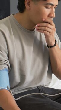Vertical video: Reacting to device reading, man wearing tee holding hand to mouth in bed with cuff
