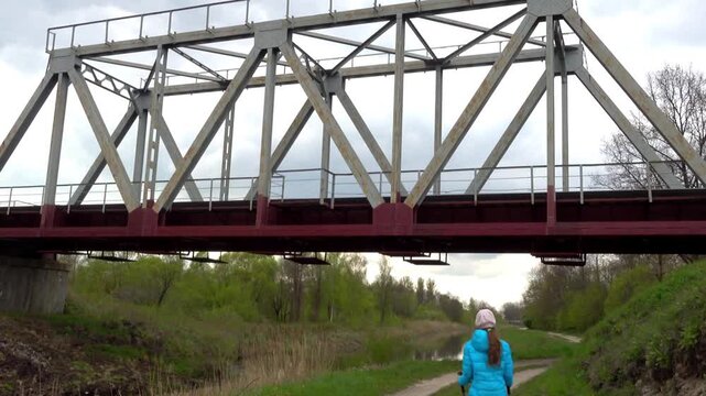 Small girl is walking under railway bridge
