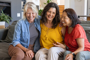 Obraz premium Diverse female friends sitting on large gray sofa at home, showing tassel blouse and smartwatch