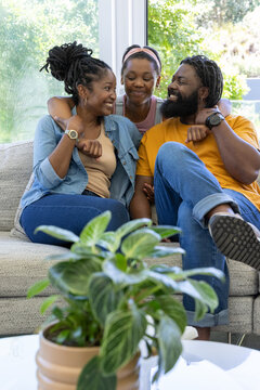 Family sitting on light sofa near vertical window wearing denim jacket and mustard tee, embracing