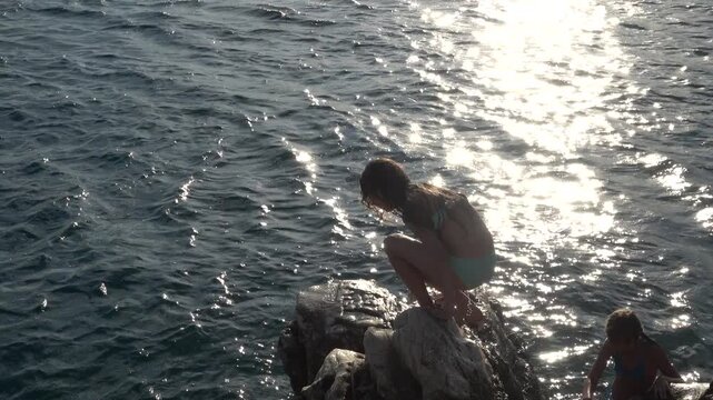 Little beautiful girl jumping from stone to sea