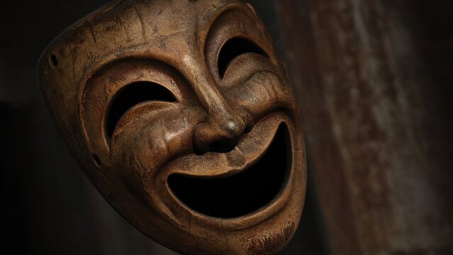 Vintage wooden theater mask with exaggerated smile, dramatic side lighting on textured surface.