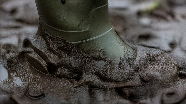 A rain boot sinking into wet, dark mud, with rich mud oozing up around its edges.