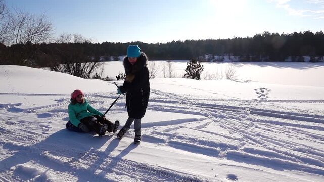 Slow motion beautiful girl in a winter jacket rolls her sister's on inflatable wheel in the snow.