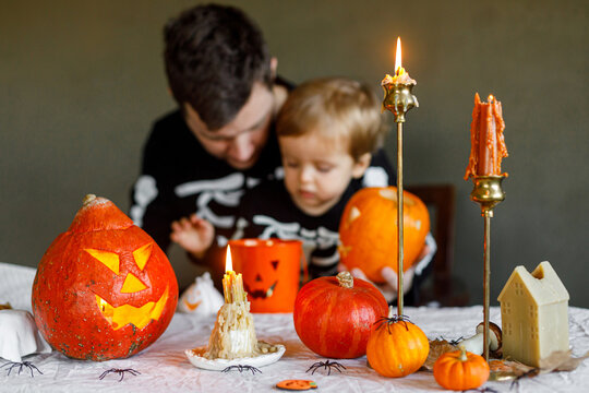 Happy Halloween. Halloween pumpkins and candles on table on background of dad and son in skeleton costumes cutting jack o lantern together, making scary decorations. Space for text.