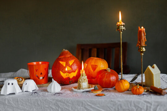 Carved halloween pumpkins, ghosts, spiders and glowing candles on rustic table on dark background, copy space. Making halloween jack o lantern and spooky decor. Happy Halloween!