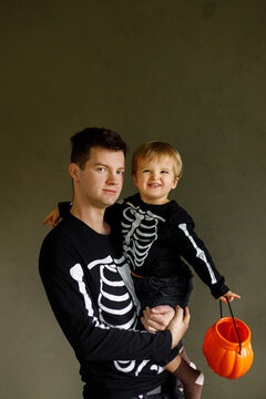 Dad and son in skeleton costumes standing with halloween candy bucket on dark background. Happy Halloween. Father with child trick or treat