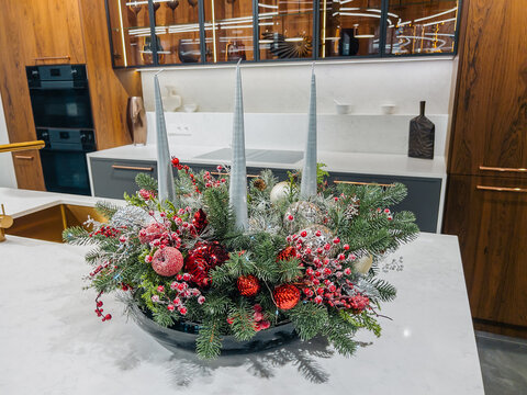 Elegant festive evergreen centerpiece with red berries and three gray candles on modern kitchen island
