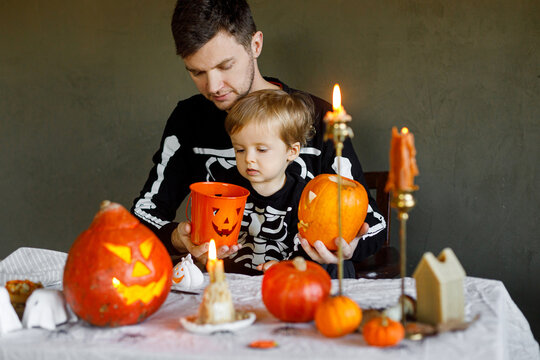 Happy Halloween. Father with child carving halloween pumpkin on table, making scary decorations on dark background. Space for text. Dad and son in skeleton costumes cutting jack o lantern together