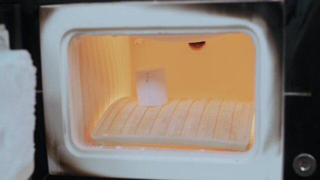 Dental technician placing a ceramic tooth crown into a hot muffle furnace for firing