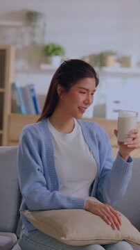 Young woman with milk glass smile cardigan at home on couch with pillow indoor lifestyle calm relaxed drinking beverage cozy room sofa portrait dairy comfort