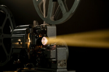 Fototapeta premium Old film projector shows light beam in dark room during movie screening