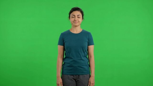 Young woman standing still and smiling in front of a vibrant green screen, expressing calmness and contentment