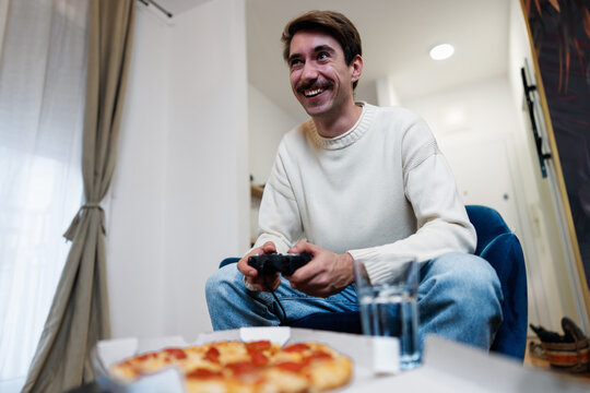 Smiling young man holding a controller and playing video games in his living room.