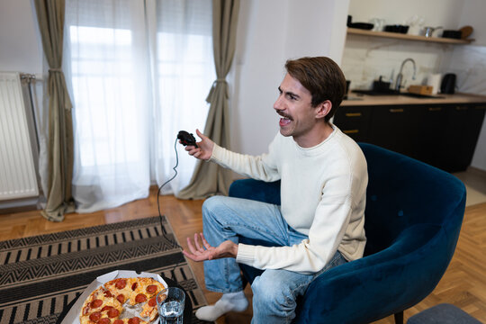 Smiling young man holding a controller and playing video games in his living room.