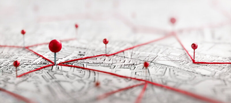 Close-up of a city map with red push pins connected by red thread, illustrating a network of locations, routes, logistics, planning, navigation, travel, business connections, geographic data