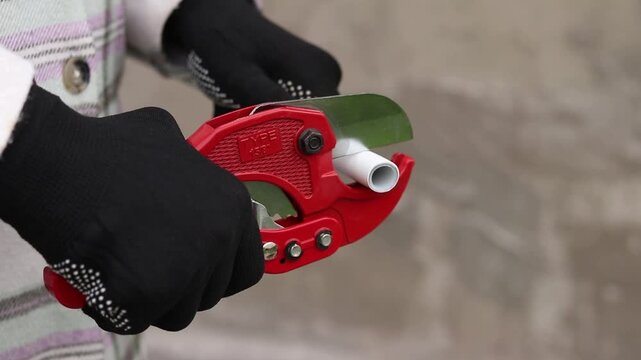A craftsman in protective gloves cuts a polypropylene pipe using a manual pipe cutter. The process of installing plastic pipes for water supply. Manual ratchet pipe cutter for PVC and PPR pipes