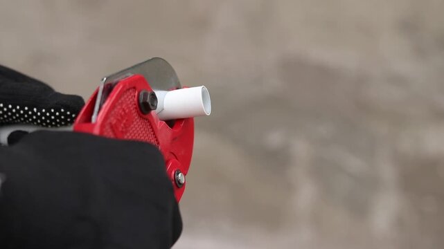 A craftsman in protective gloves cuts a polypropylene pipe using a manual pipe cutter. The process of installing plastic pipes for water supply. Manual ratchet pipe cutter for PVC and PPR pipes