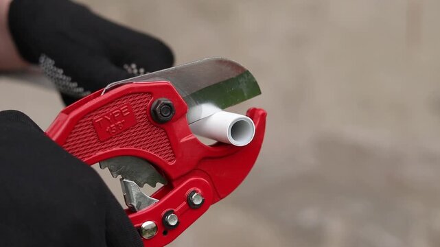 A craftsman in protective gloves cuts a polypropylene pipe using a manual pipe cutter. The process of installing plastic pipes for water supply. Manual ratchet pipe cutter for PVC and PPR pipes