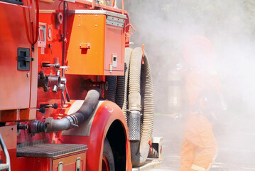 Naklejka premium Fireman prepare equipment fighting extinguisher at fire engine truck. Firefighter fighting with smoke flame using fire hose, tube, chemical water foam spray at truck. Fireman wear hard hat protection