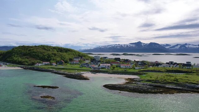 Aerial of small traditional village with greenery covered mountain background, on summer Sommaroy island, Norway