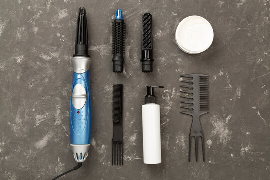 Hair styler with care products on concrete background, top view