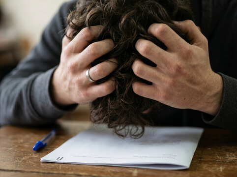 Frustrated person clutching hair over test paper on desk closeup