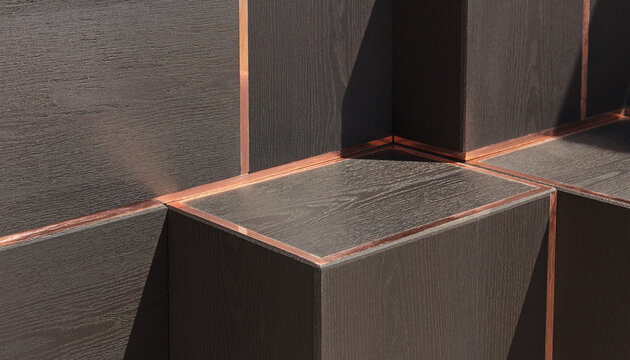 Minimalist geometric background of dark matte finished oak wood blocks inlaid with thin flush lines of brushed copper metal texture