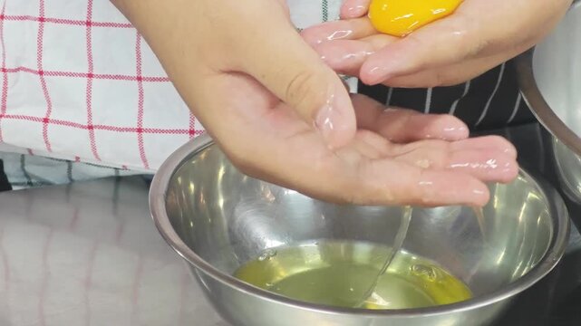 Close up of hands separating a raw yellow egg yolk from the white.