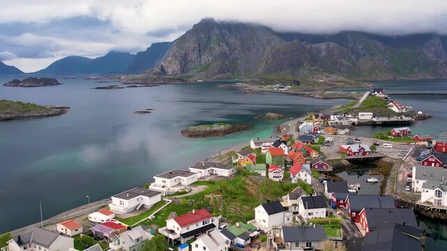 Aerial of small traditional town Henningsvaer with greenery covered mountain background, on summer Lofoten island, Norway