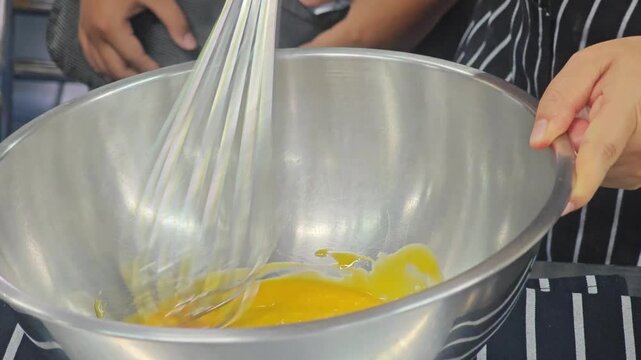 Whisking raw egg yolks in a stainless steel bowl.