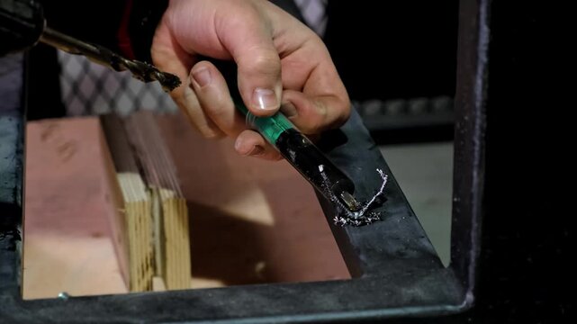 Lubricate with oil from a syringe before drilling a hole in the metal. Details of Industrial process. B-roll. High quality 4k footage.
