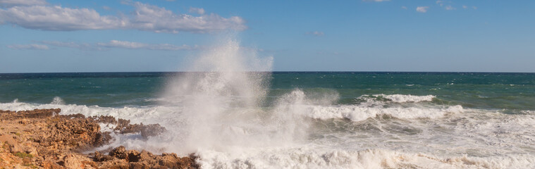 Fototapeta premium Powerful surf hitting rocks emerald blue sea white foam and clear sky