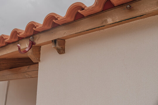 Low angle view of a ceramic tile roof edge with an empty metal bracket on a stained wooden beam, where the drainage gutter has completely fallen off due to damage