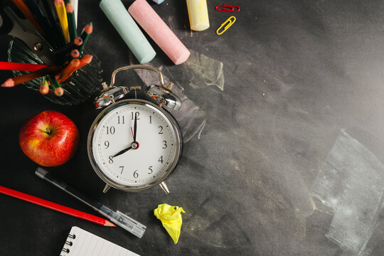 Blackboard workspace with school supplies and alarm clock, education background, back to school concept