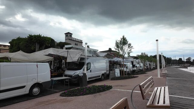 Bardolino, Italy - May 14, 2026 - Waterfront market stalls with vans and boats docked nearby under cloudy skies