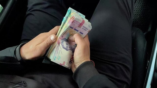 hands of man in car folding cash of hryvnia. colorful Ukrainian banknotes, counting currency with focus on cash and financial concept, person in casual clothing managing money, realistic banking scene