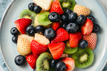 Obraz premium Fresh fruit salad in a plate, kiwi slices, strawberries and blueberries. Healthy food, sweet dessert, top view
