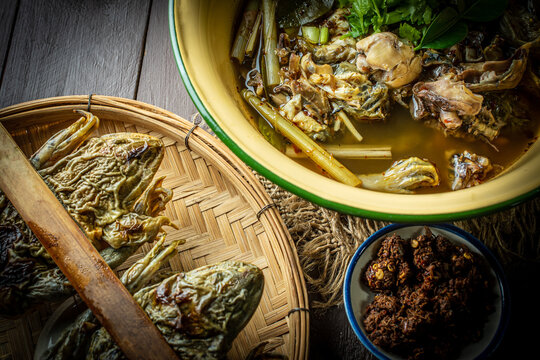 Northern Thai spicy frog soup with local herbs and vegetables, served in a yellow zinc bowl on a rustic wooden background, top view food photography. 