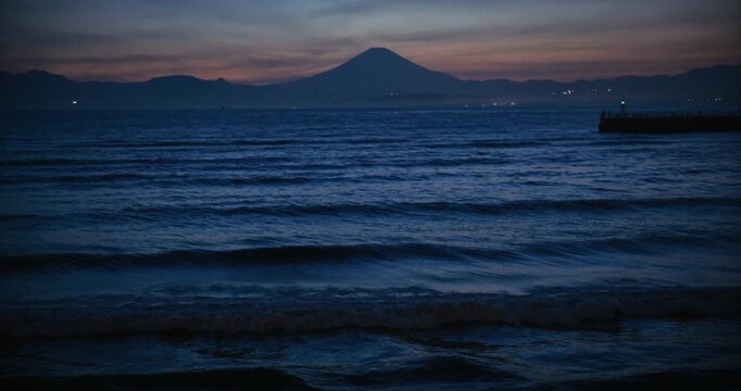 Tilt, zoom in shot on rippling waves at dusk with distant hills