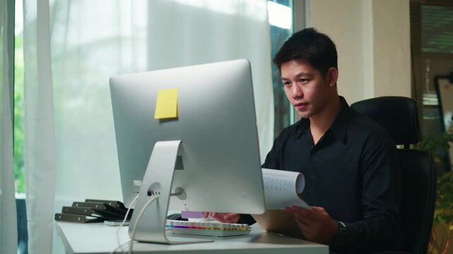 4k Young Asian Businessman Reading Documents at Computer Desk in Modern Office