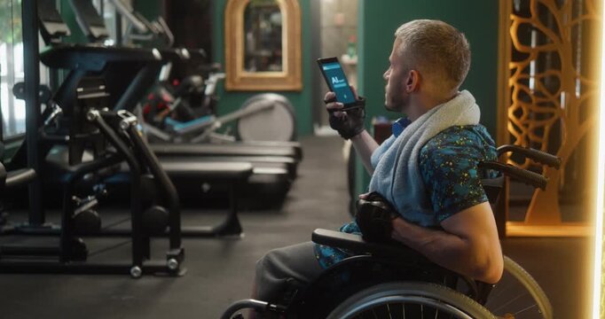 Man in a wheelchair talks to an AI assistant on his smartphone during a workout session in the gym. The technology helps him receive exercise guidance and stay motivated while maintaining an active li