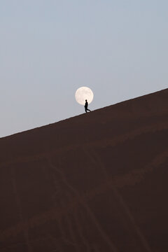 Silhouette of man on sand dune with full moon, Dunhuang desert, Gansu, China