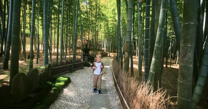 Boy with Backpack Walking Toward Camera Through Bamboo Forest Path In Japan - Slow Motion
