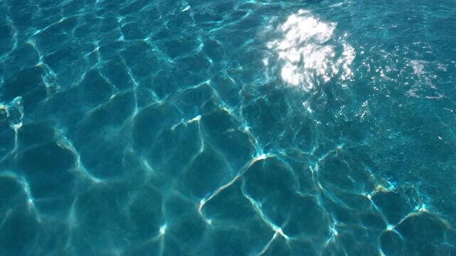 Vibrant clear blue water surface with mesmerizing sunlight patterns and subtle ripples, perfect for abstract backgrounds, summer themes, relaxation, aquatic textures, and tranquil video projects.