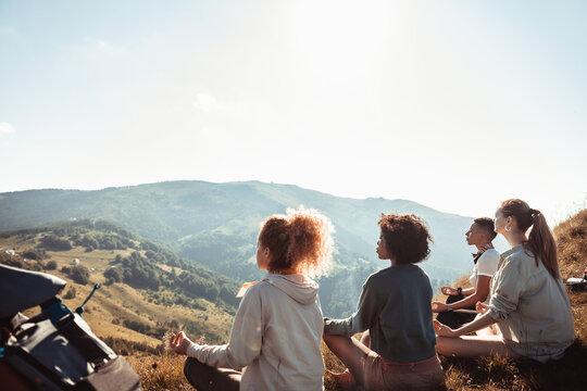 Group of friends meditating on mountain hillside during hike