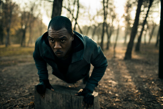 Athlete performing incline push-ups on tree stump in forest park