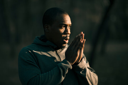 Man in hoodie warming hands outdoors at dawn